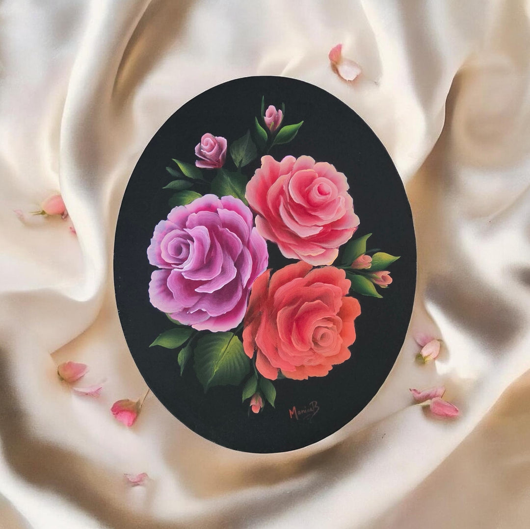 Round painting of pink and red roses on a black background, placed on a white fabric surface.